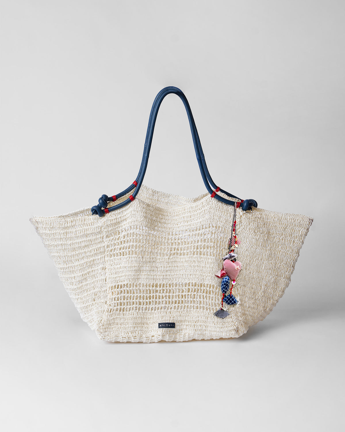 Cream open-weave Riya tote with navy leather handles and a heart charm.