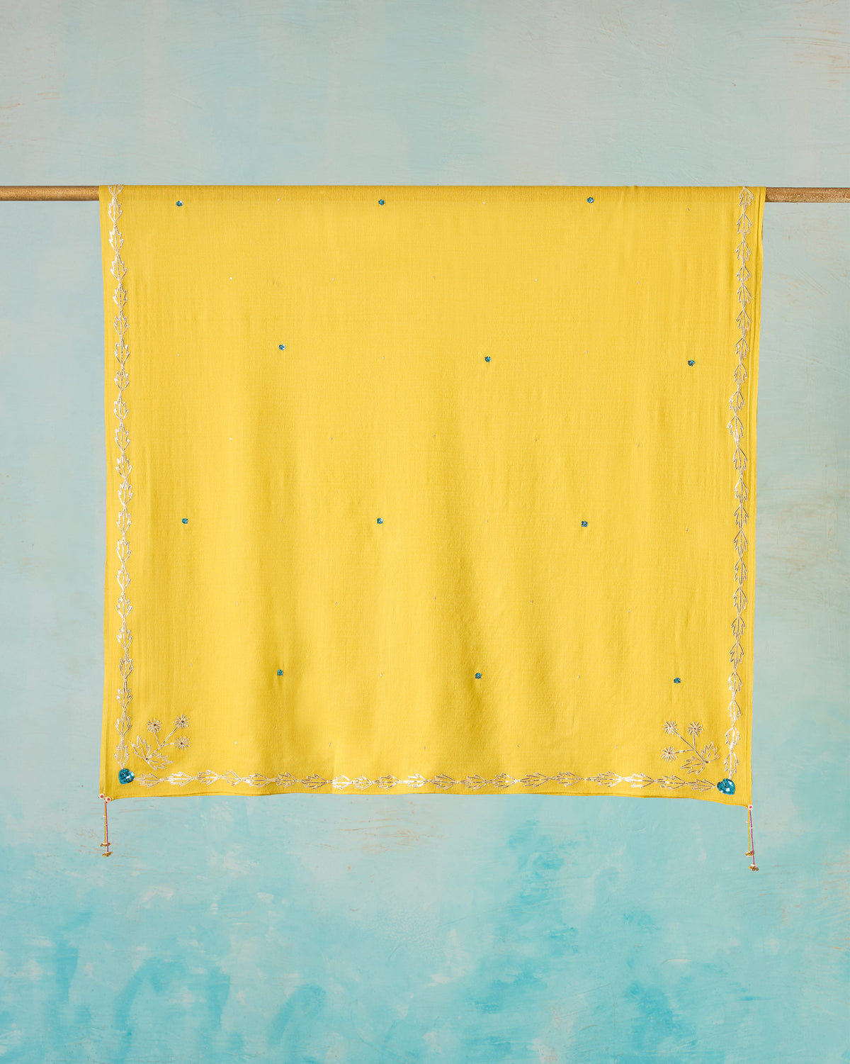 Yellow Saanjh shawl hung flat, with embroidered edges and teal sequin accents.