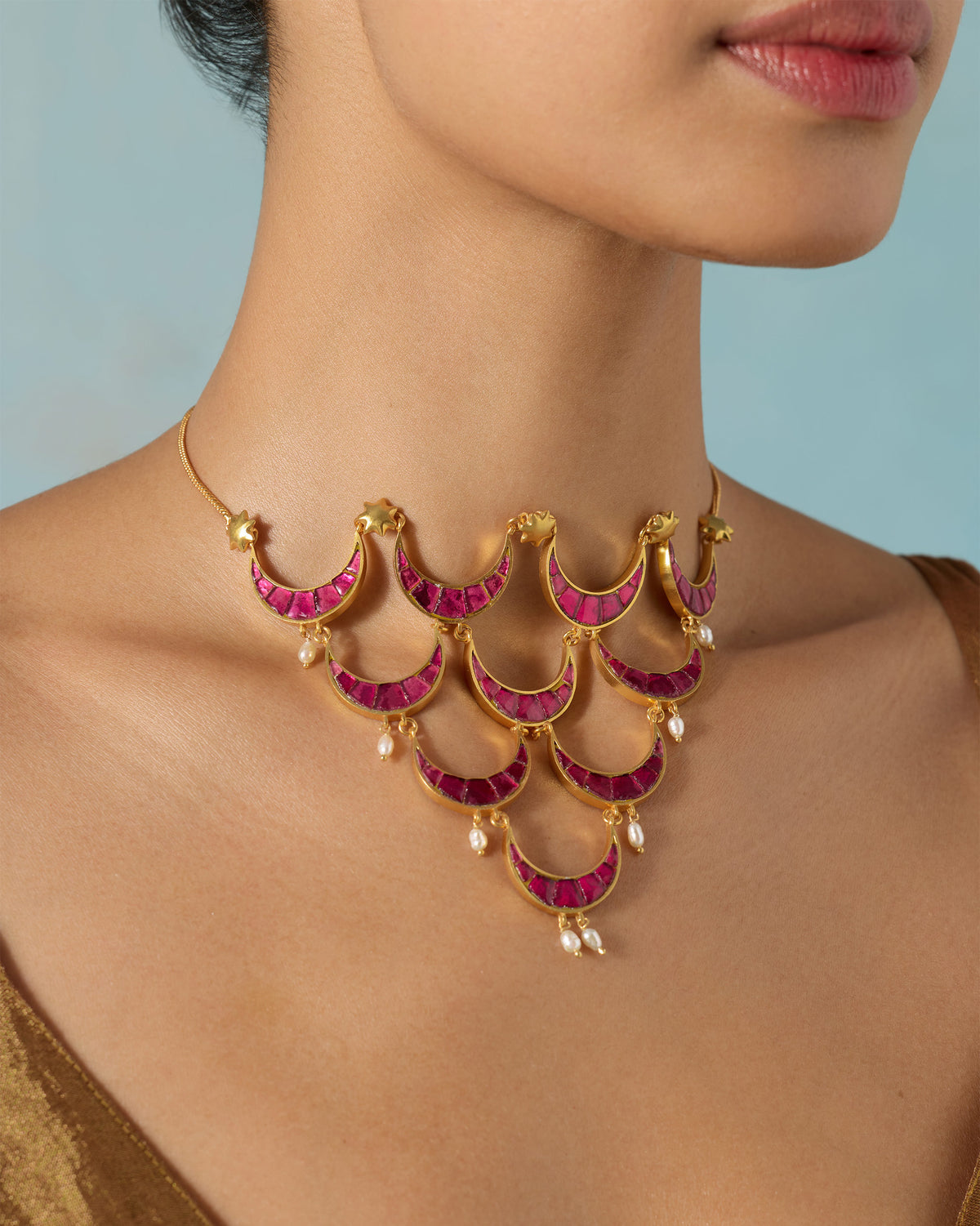 Close-up of a person's neck wearing a gold Gul-Chand necklace with pink crescents.