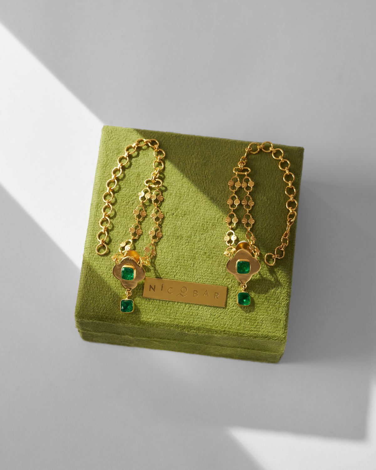 Gold Clover Kanauti earrings with green stones laid on a green box.