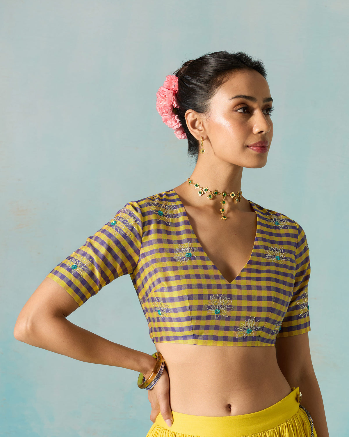 Person wearing a yellow and purple checked Dori blouse with embroidered flowers.