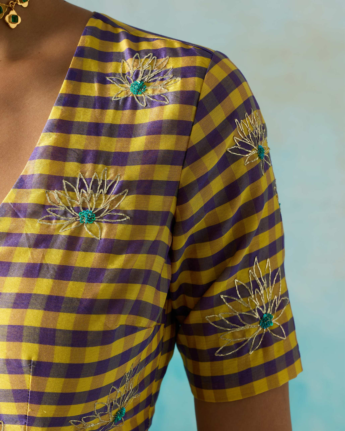 Close-up of a checked Dori blouse showing white embroidered flowers with green centres.