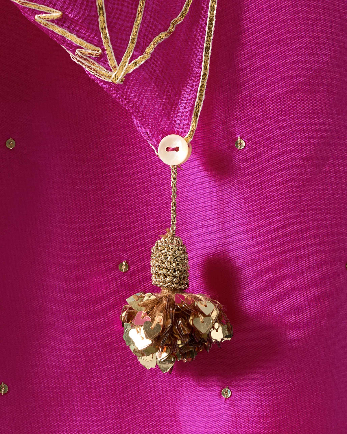Close-up of a gold sequin tassel and button on a magenta Ishara dupatta.