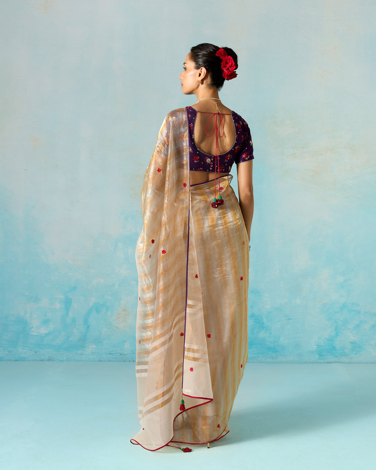 Back of a gold tissue sari with a red-piped edge, worn by a person.