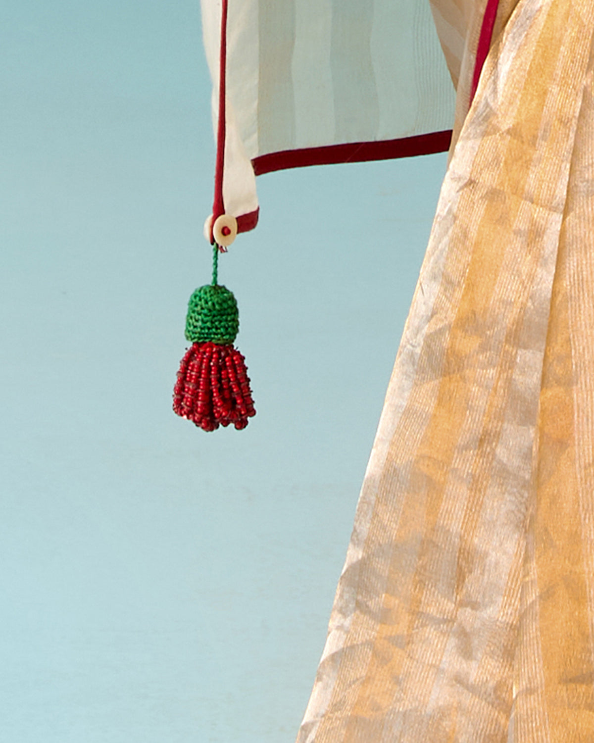Close-up of a red and green beaded tassel on the edge of a gold tissue sari.