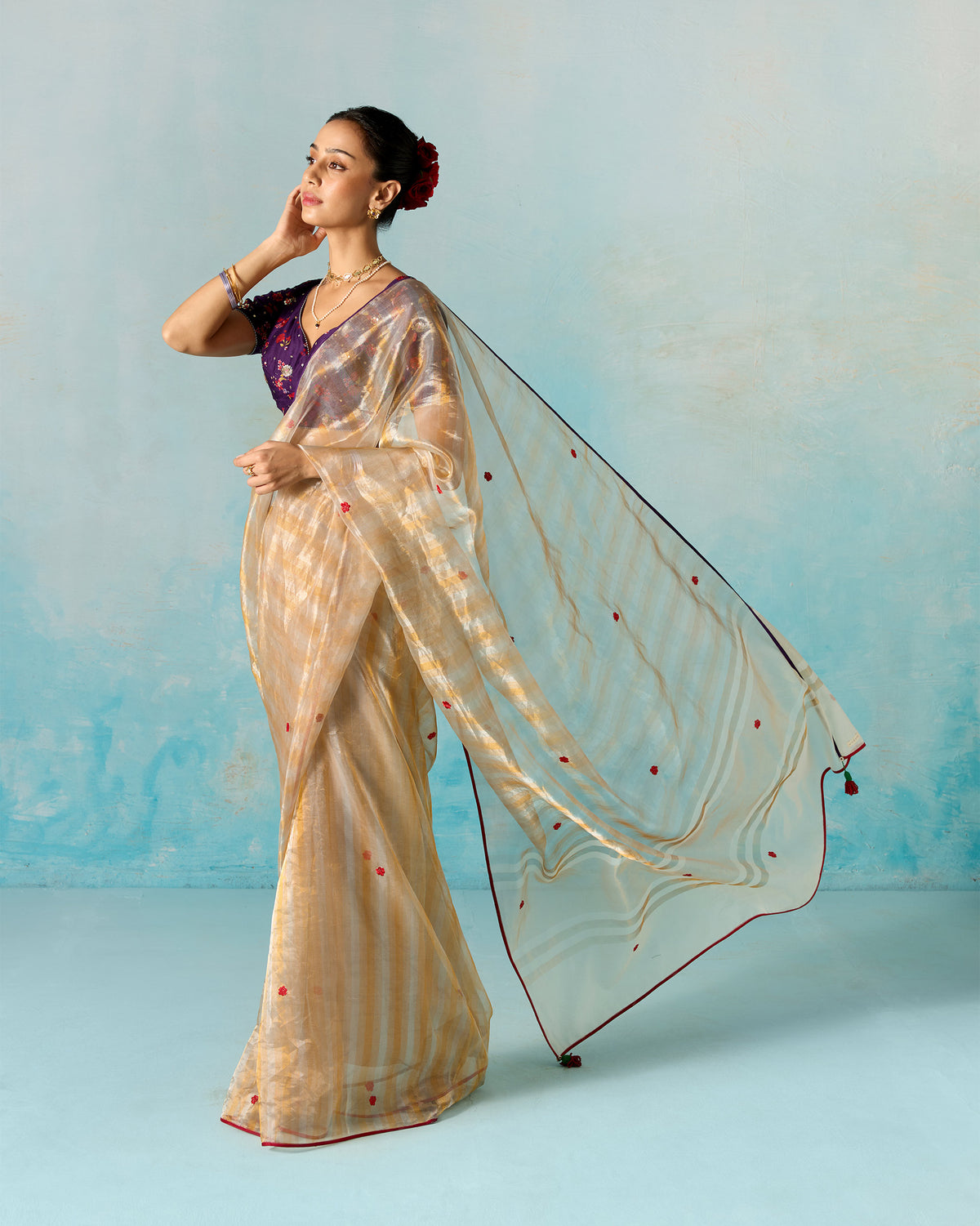 Side view of a gold tissue sari with a long sheer drape worn by a person.