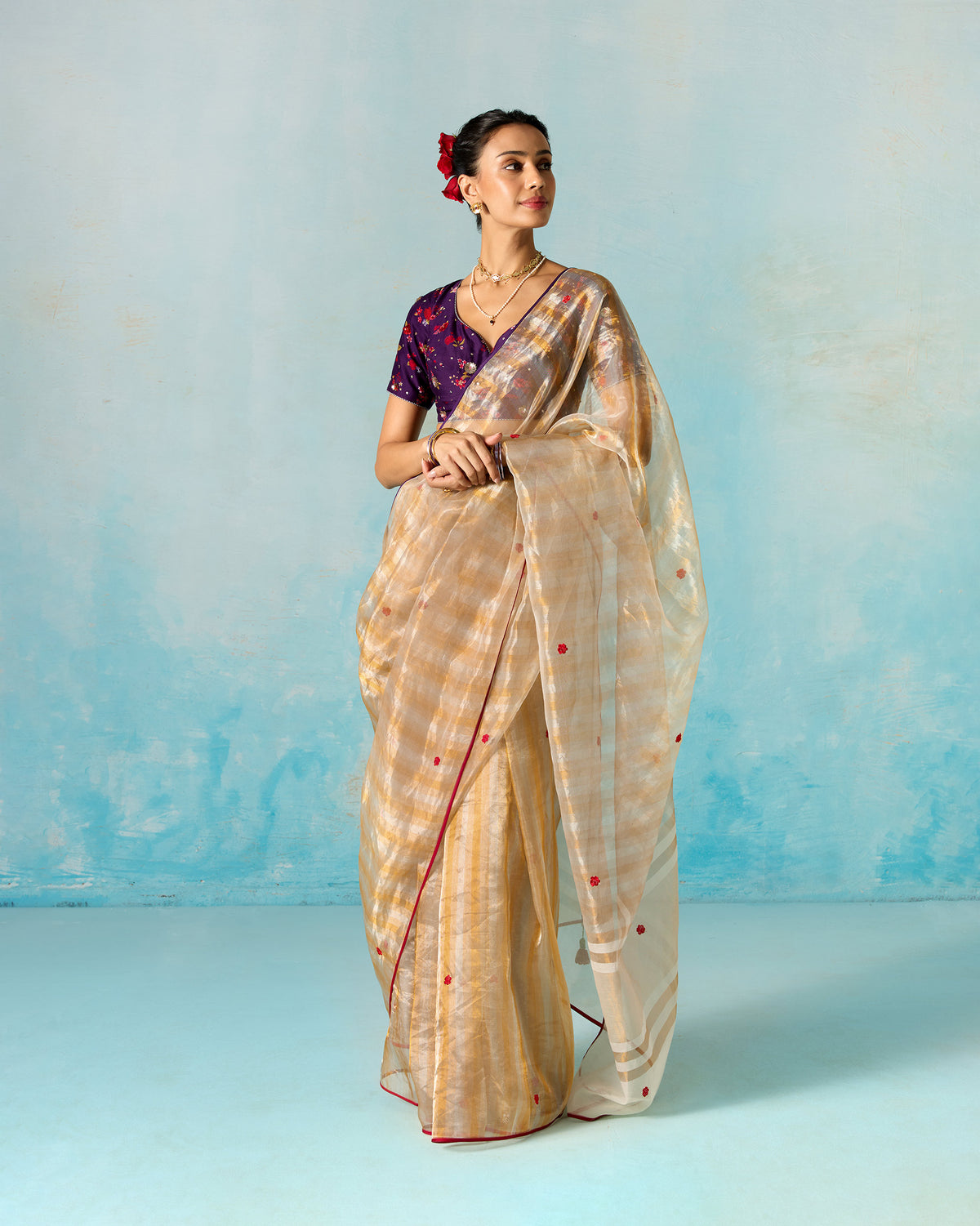 Person standing wearing an embroidered gold tissue sari with red dot motifs.