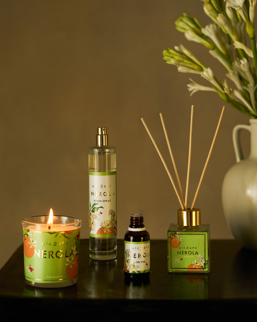 A lit Nerola candle with the room spray, oil vial and reed diffuser on a table