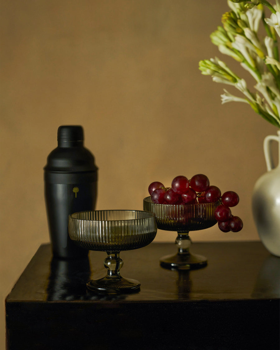 The black Avi shaker and smoked coupe glasses with grapes on a dark table