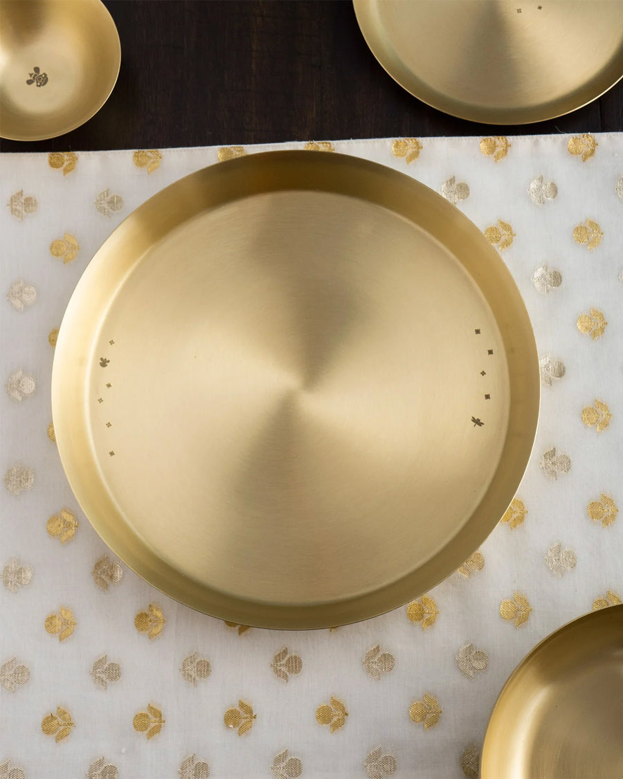 The brass Madhu thali on a patterned cloth with matching pieces