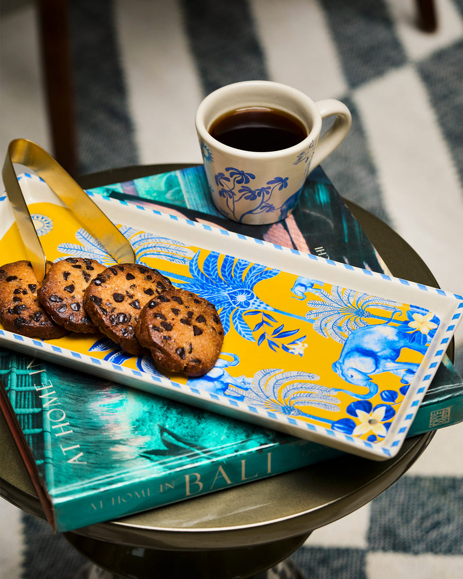 The yellow Alam tray with cookies and a gold tong beside a cup of coffee