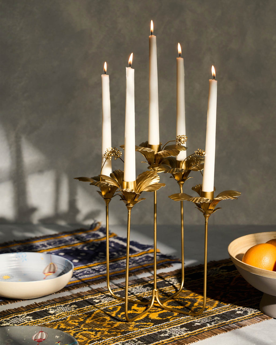 The gold hibiscus candle holder with five lit tapers on a patterned runner