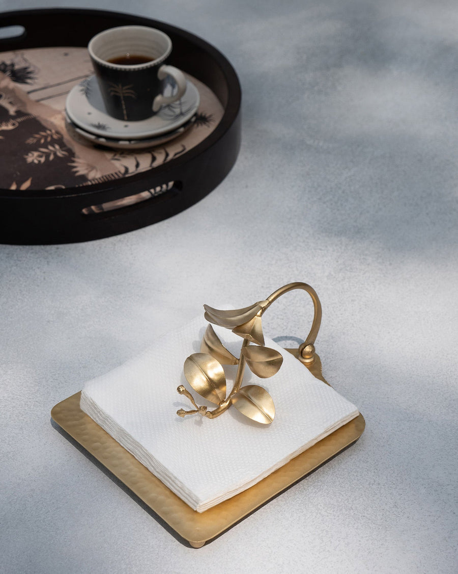 The gold clove branch holder weighting white napkins beside a tray of coffee