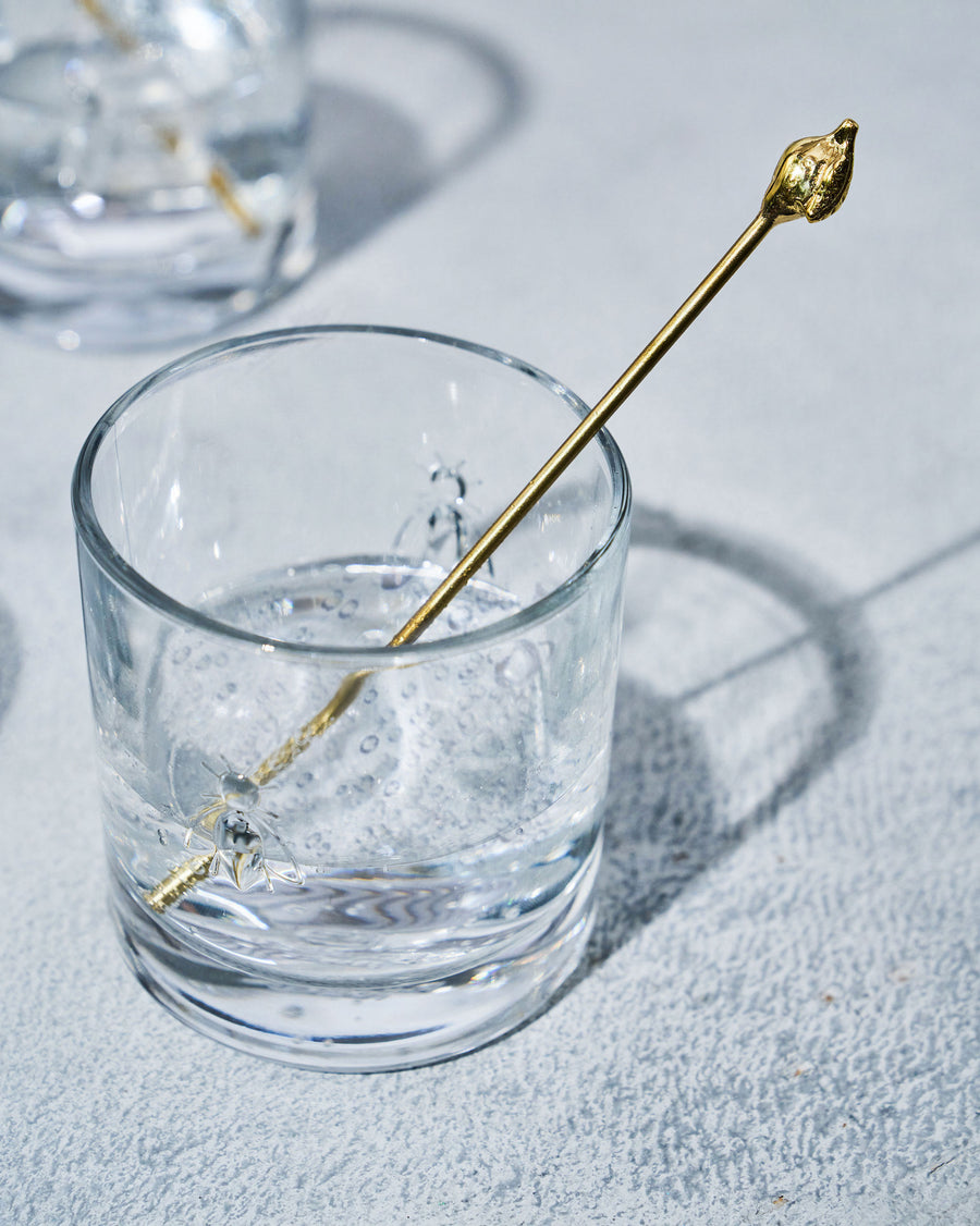 A Bumble Bee glass with a gold stirrer in bright light