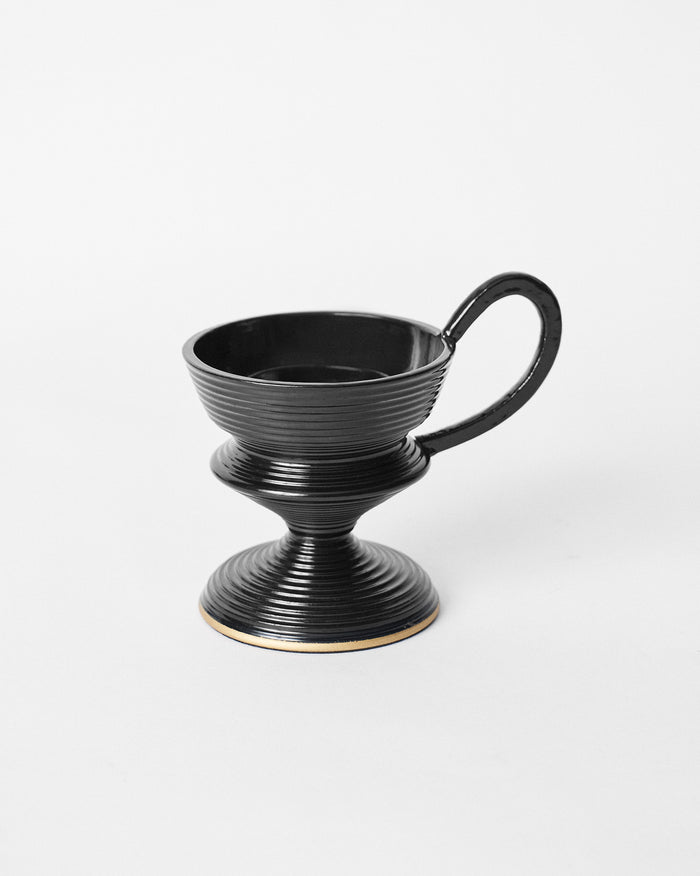 Black ribbed Ataraxy dhuna with a pedestal base and curved handle.