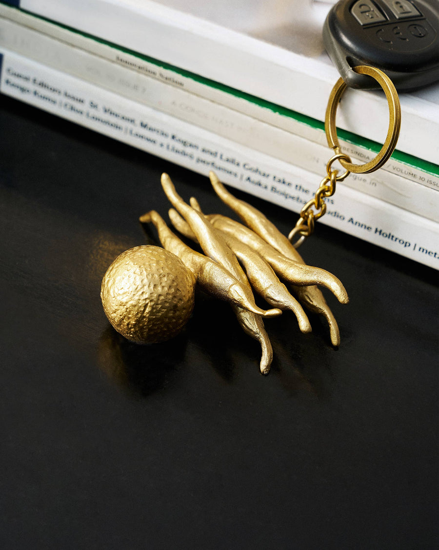 The gold nimbu-mirchi keychain on a dark table beside a car key and books