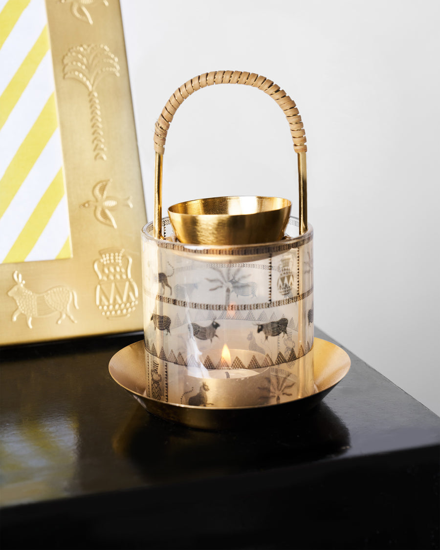 The lit Indus diffuser with its rattan handle beside a gold frame