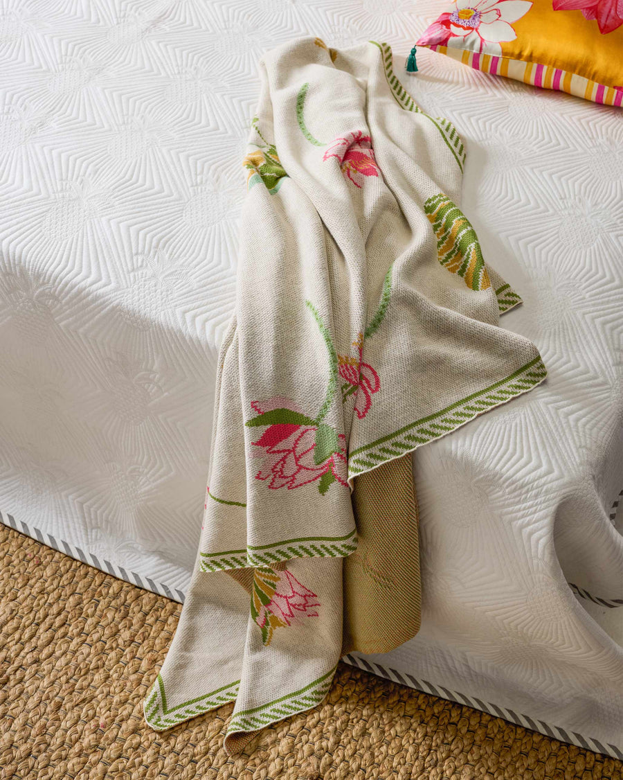 The Lily Pond throw draped over the end of a bed, pink lotuses and a green border