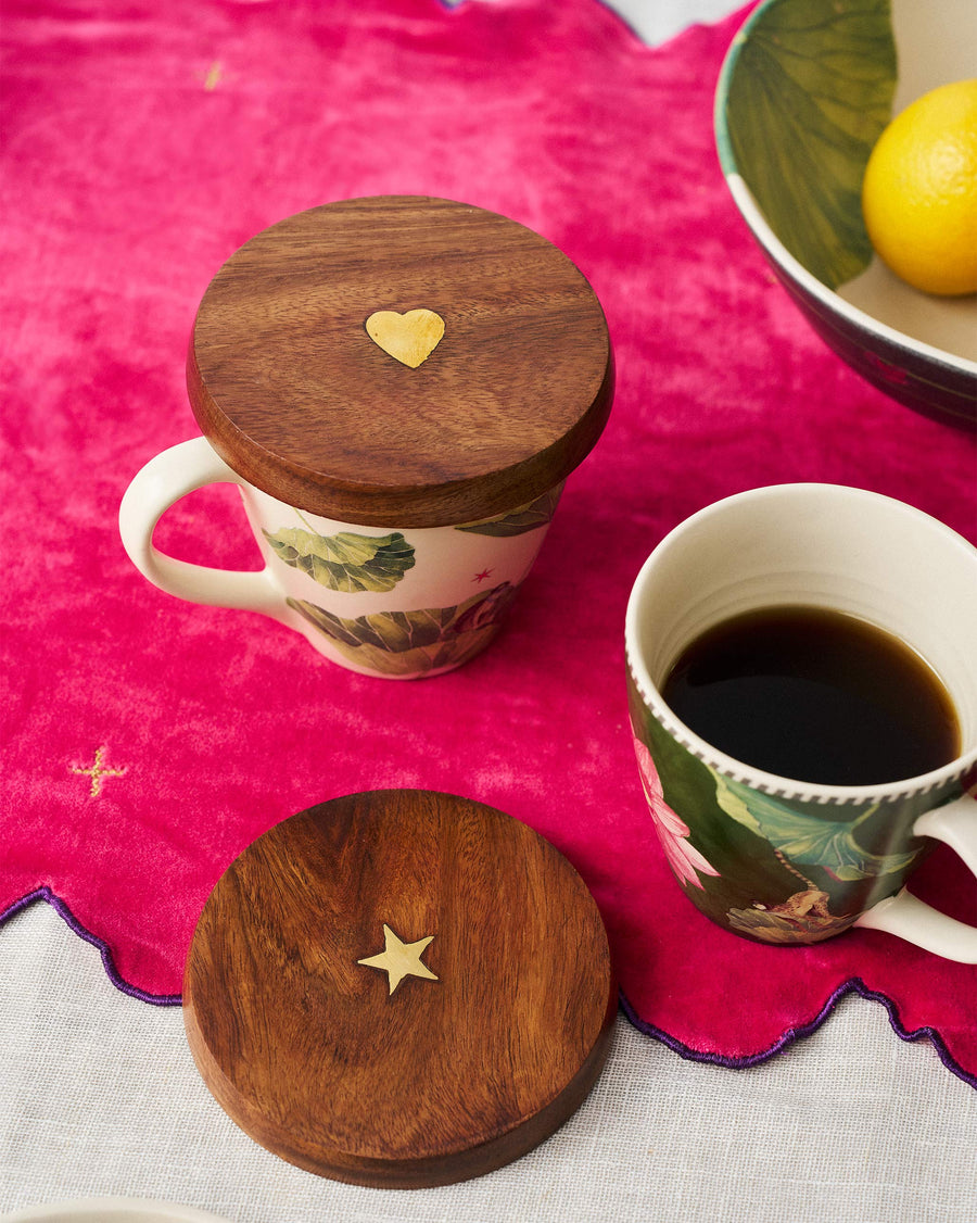 Wooden Aster lids on floral mugs on a pink cloth