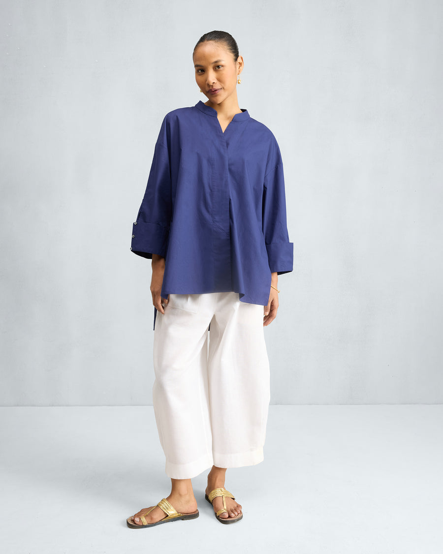 The Cirrus Shirt in ink blue, worn loose over white trousers.