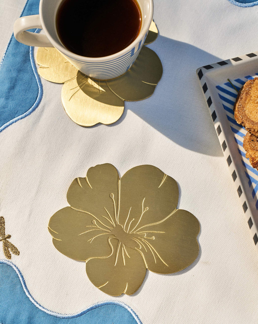 Brass almond blossom coasters under a cup of black coffee on a blue cloth