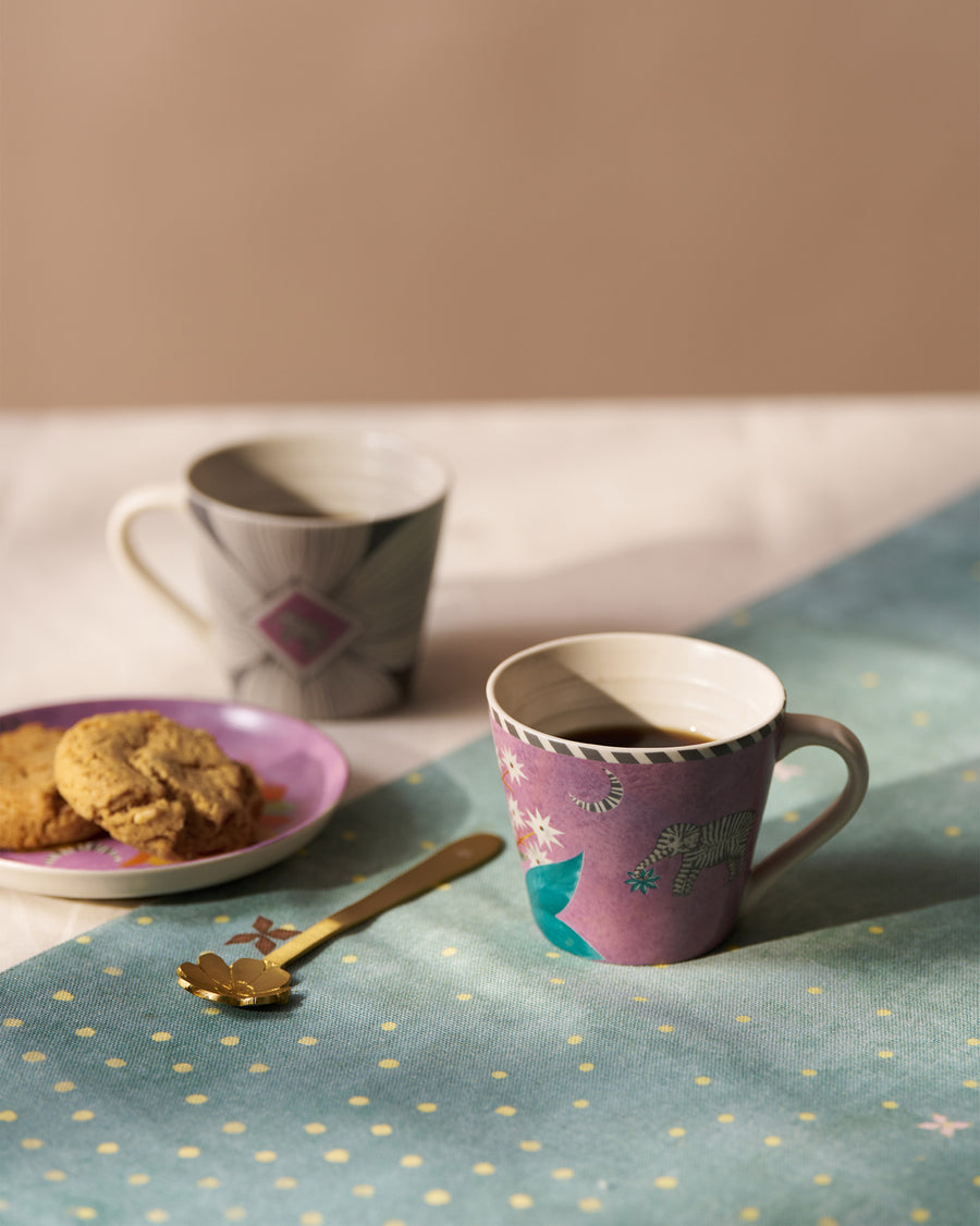 Two Mogra Bloom mugs with coffee and a plate of biscuits on a starry runner