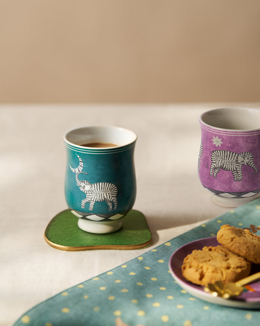 A teal Tusk cup of tea on a green coaster beside cookies