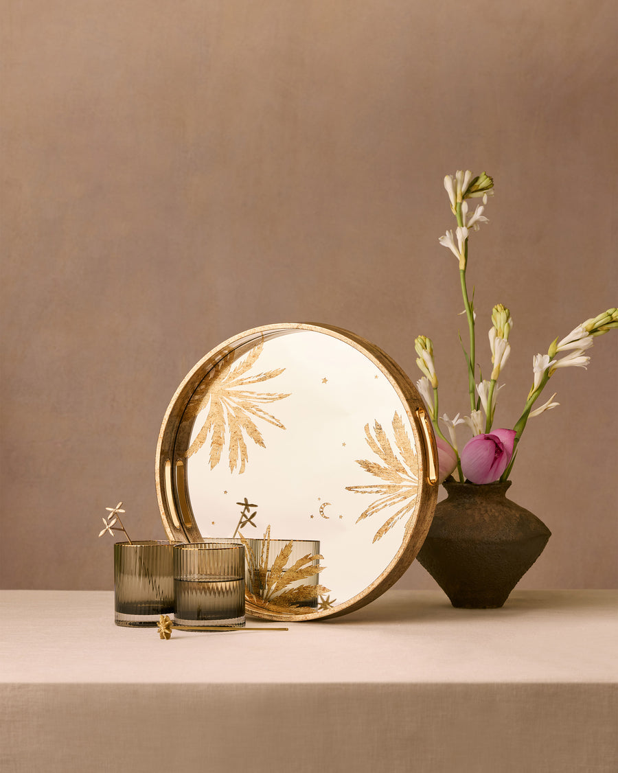 The Gilded Palm tray and glasses on a table beside a vase of flowers