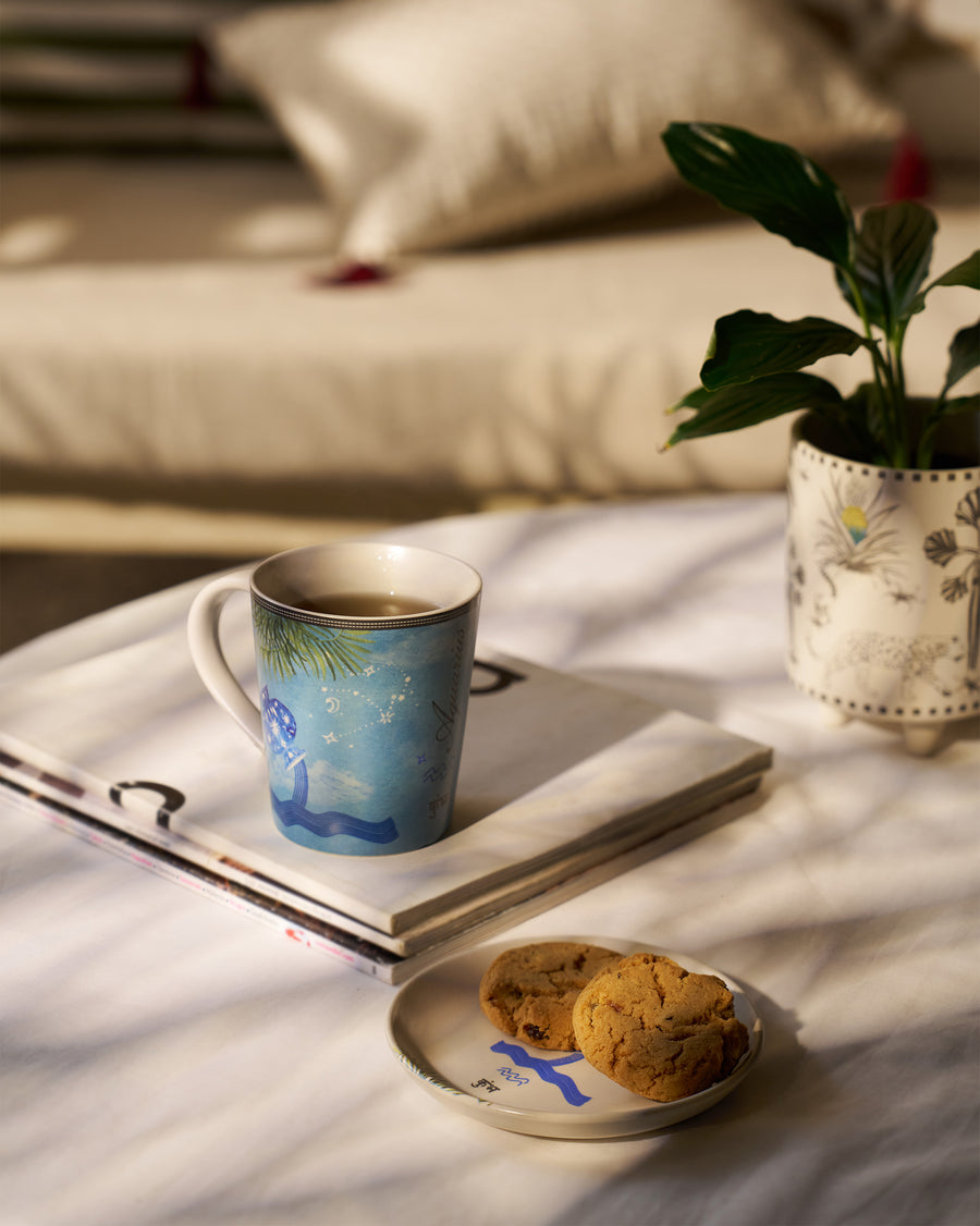 The Aquarius mug on a book beside a plate of cookies