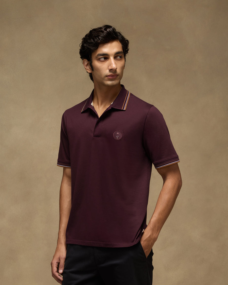 The Stag Polo T-Shirt, front view: a maroon mercerised cotton polo with a tipped collar and a round label at the chest.