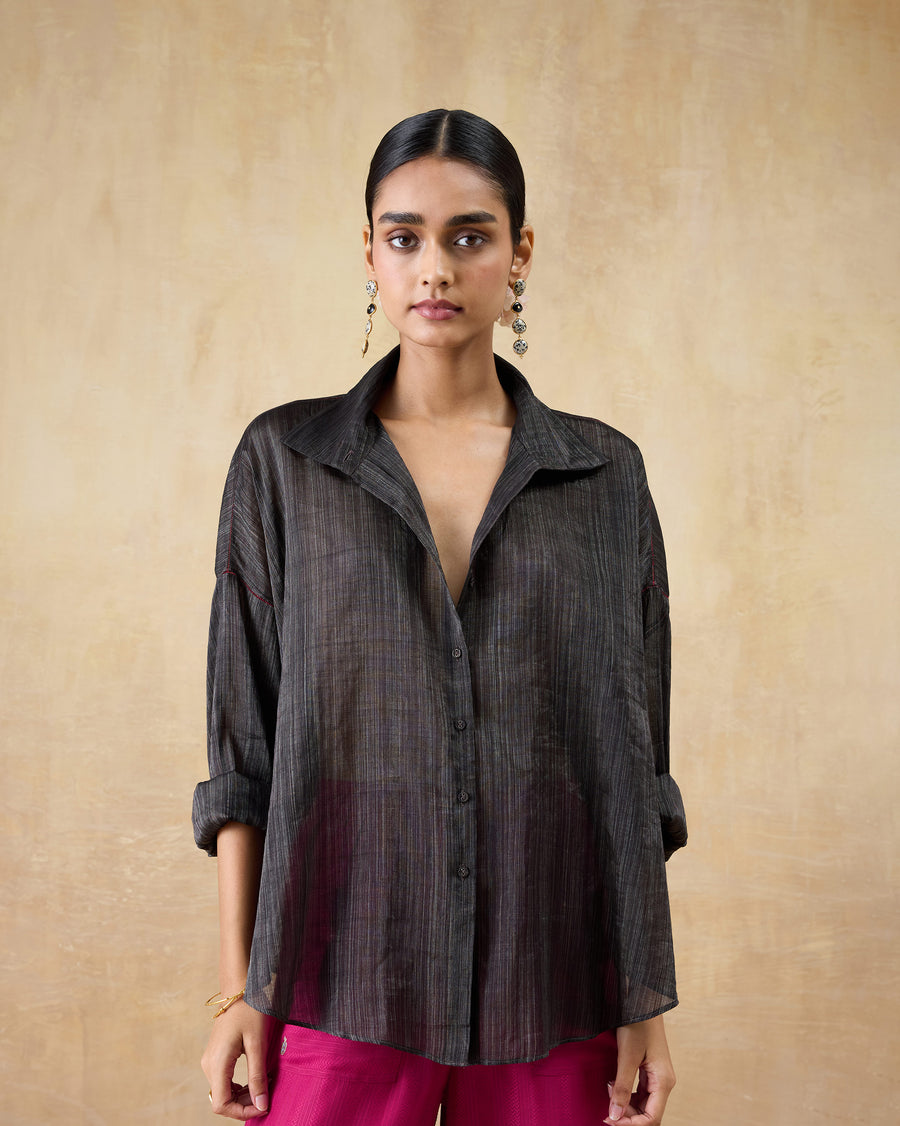 The Firefly Shirt, a loose black metallic tissue shirt with a classic collar, worn with pink trousers.