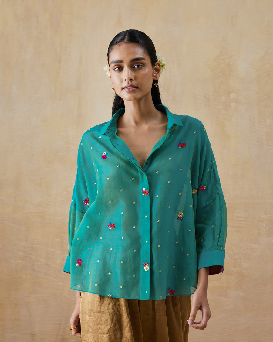 The Boxy Shirt, a loose aqua cotton silk shirt with small embroidered flowers all over, worn with gold trousers.