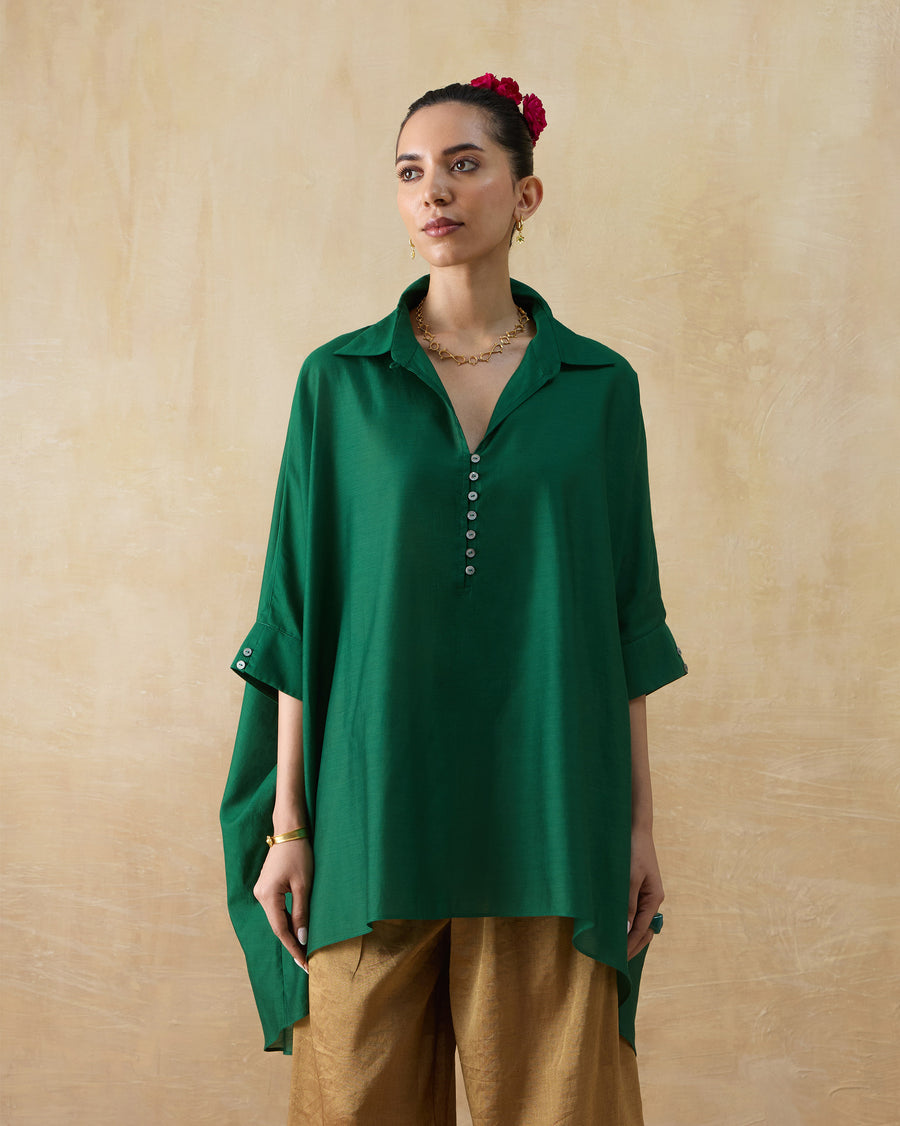 The Hala Tunic, a loose emerald green cotton silk tunic with a shirt collar and kaftan sleeves, worn over gold trousers.