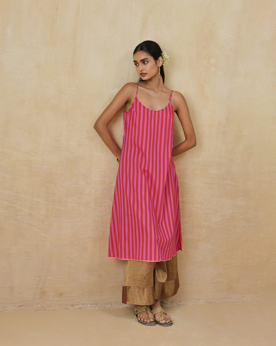 The Mist Camisole, a knee-length red and berry striped voile camisole with thin straps, worn over gold trousers.