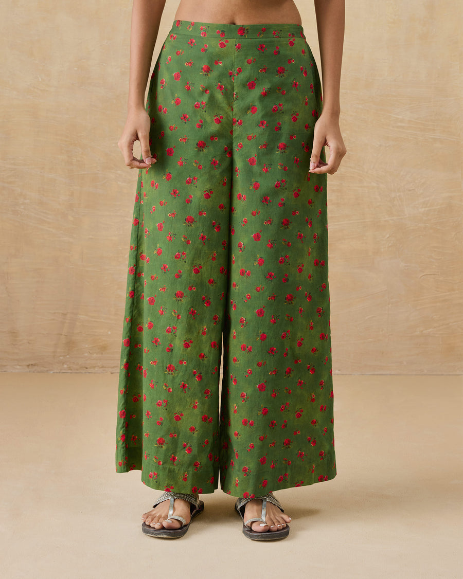 The Basic Pyjamas, wide-leg olive green organic cotton voile pyjamas with a small red floral print, worn with flat sandals.