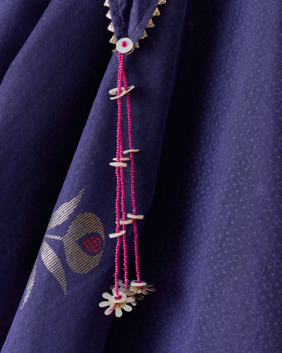 Close-up of a corner of the Buzz Dupatta, with a tassel of pink beads and shell beside a gold foil anar.