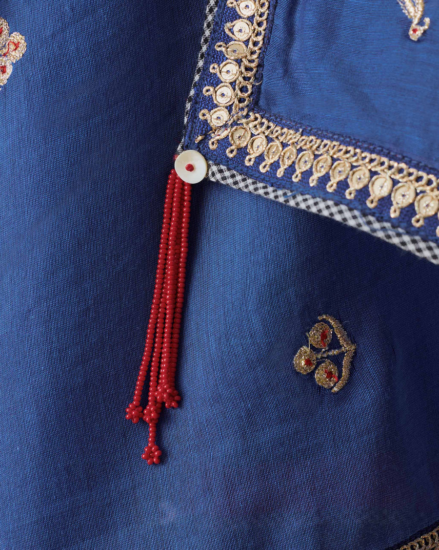 Close-up of a corner of the Leher Dupatta: a gota border edged in checked tape, a red bead tassel and a gold zari motif.