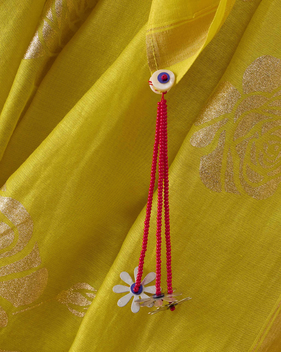 Close-up of the Sunset Sari: a red bead tassel with a daisy charm beside a gold foil rose.