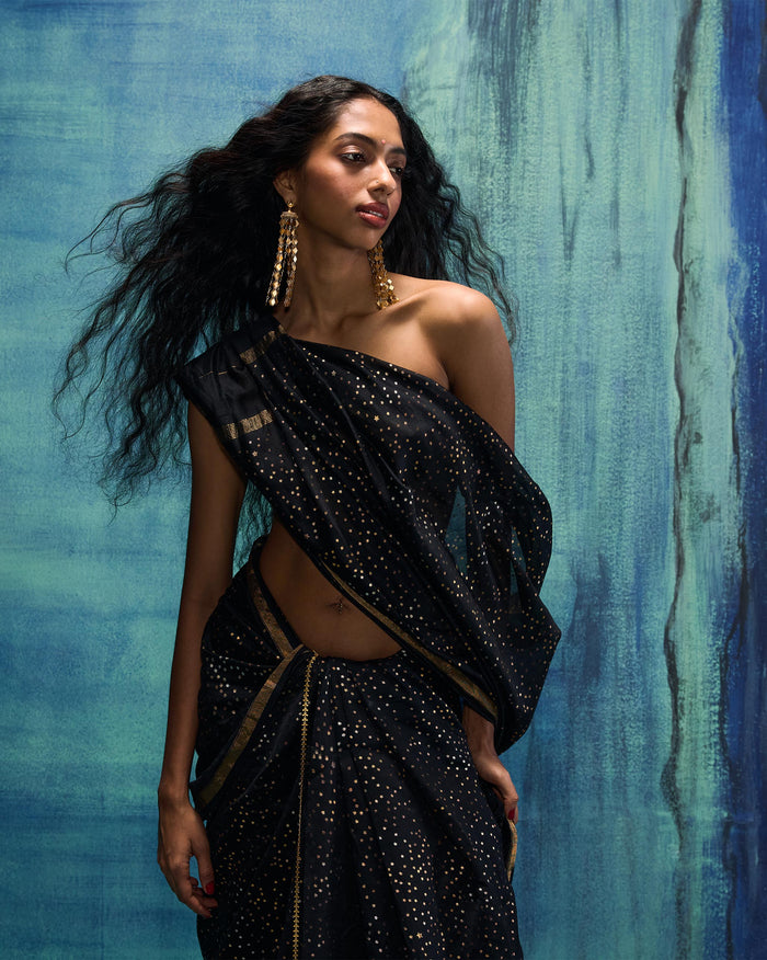 Person wearing a black and gold Riverbank sari with scattered gold dots.