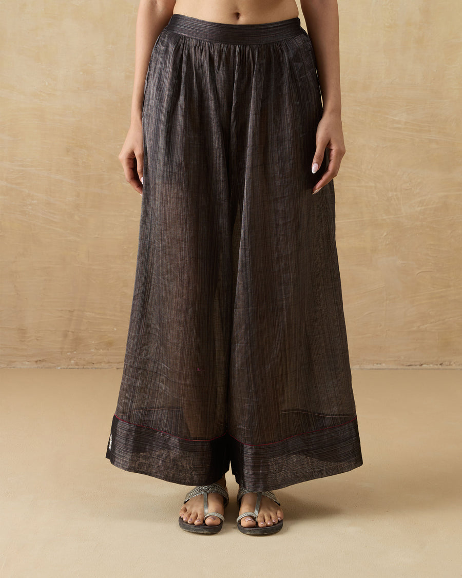 The Charisma Pants, wide-leg black metallic tissue pants with a deep hem band, worn with flat sandals.