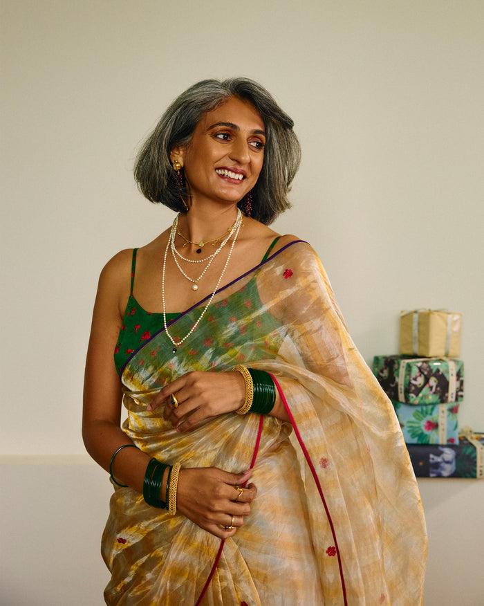 Person standing wearing an embroidered gold tissue sari with red dot motifs.
