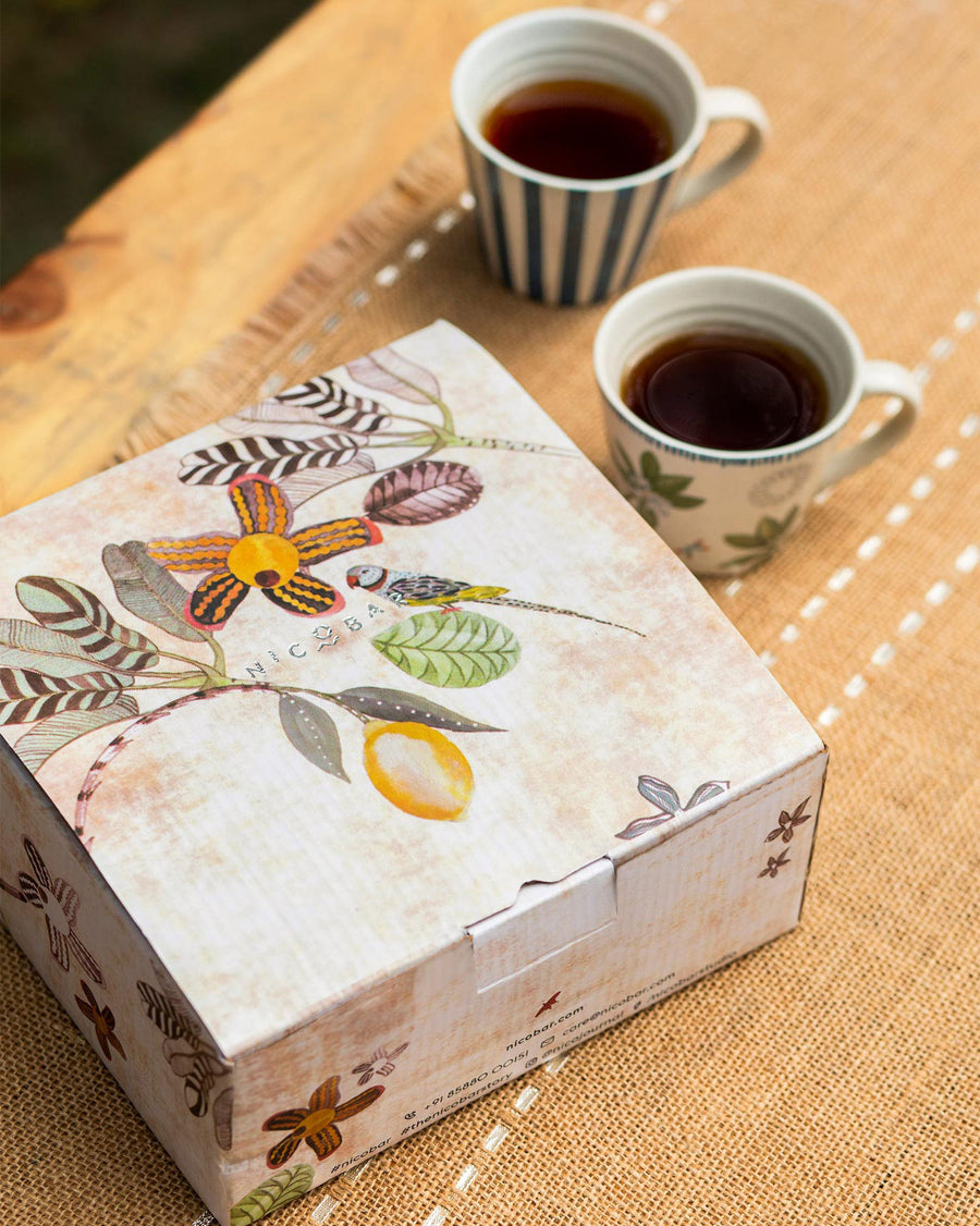 Two mugs of tea beside the botanical-print gift box