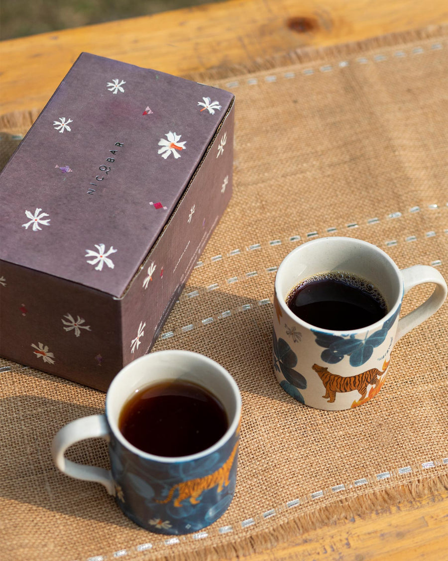 Two mugs of coffee beside a purple floral gift box