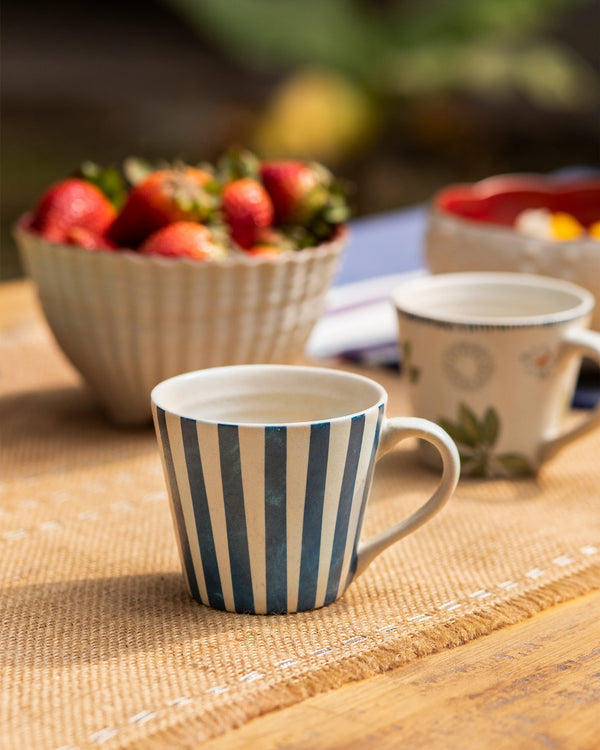 A striped mug in front of a bowl of strawberries