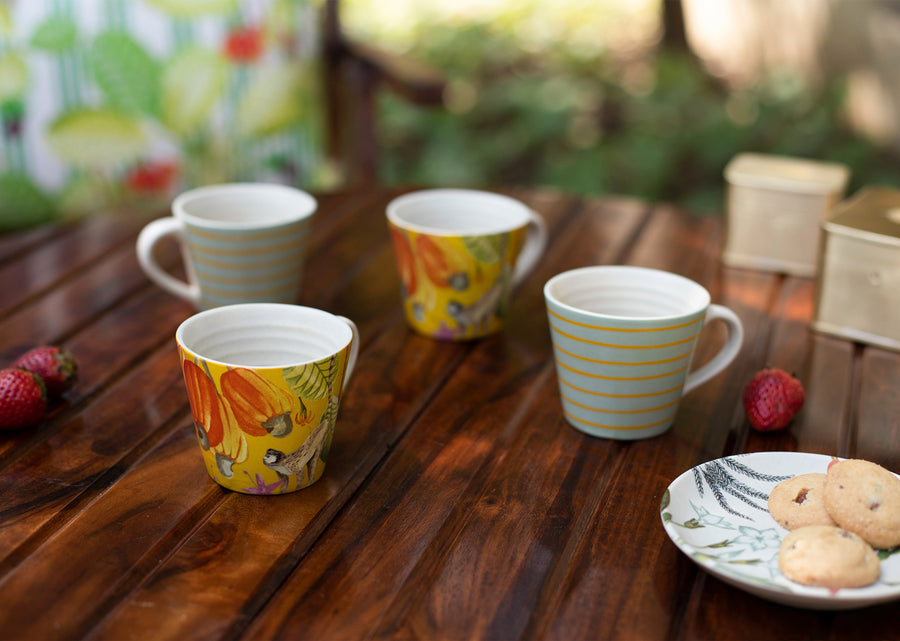 Four Mahi mugs on a wooden table outdoors beside cookies